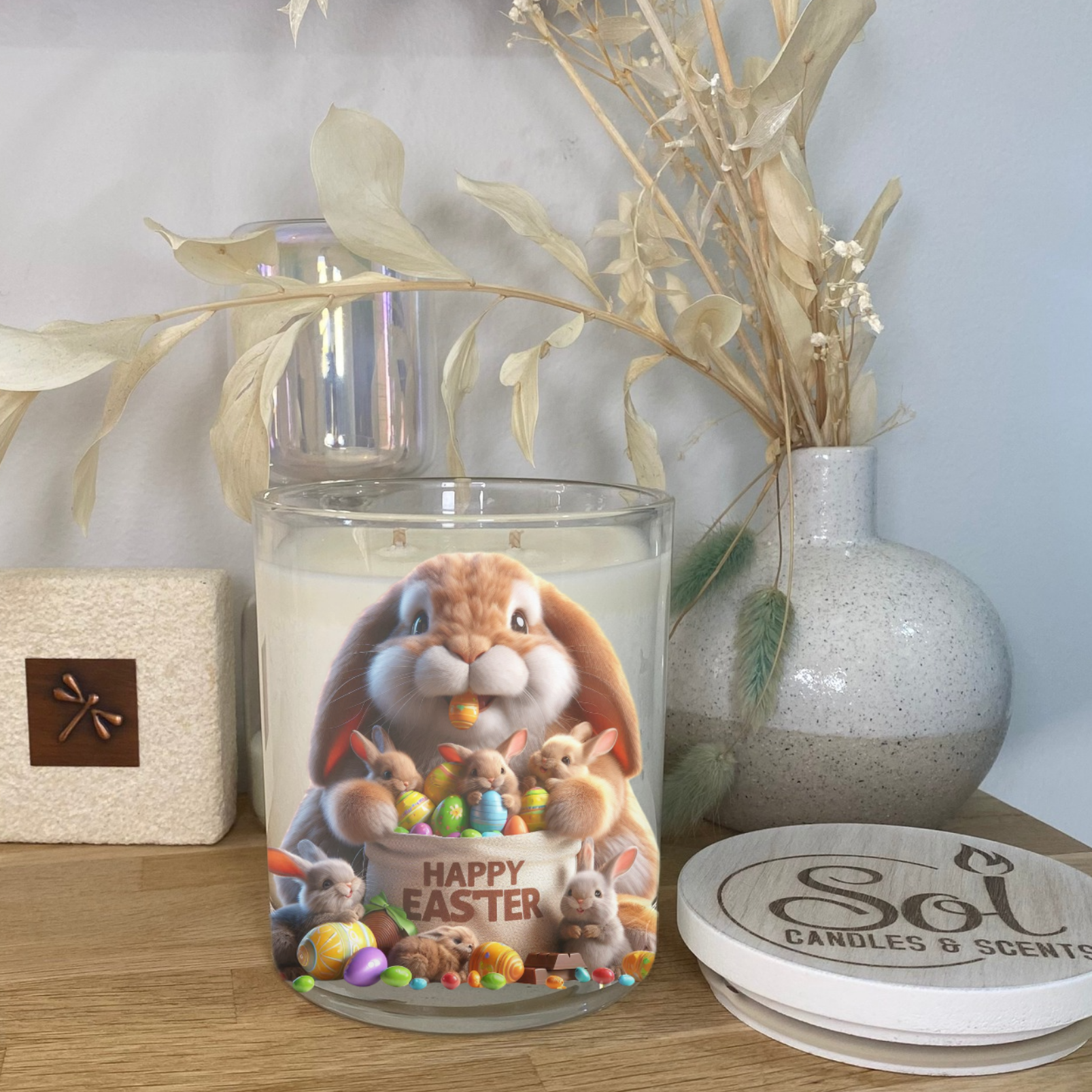 Decorative candle with Easter design on a wooden surface, featuring a rabbit and eggs.