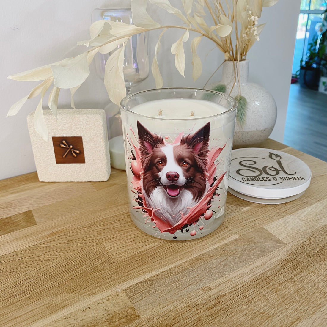 Candle with a Border Collie dog design on a wooden surface, surrounded by decorative items.