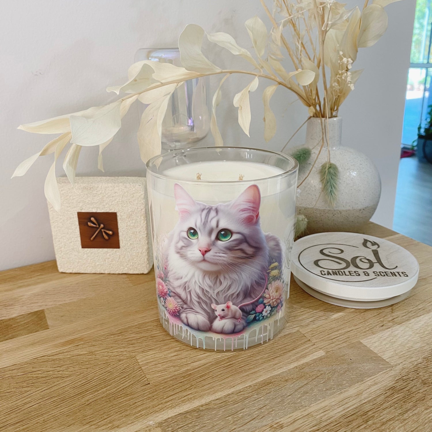 Candle with a cat design on a wooden surface, surrounded by decorative elements.
