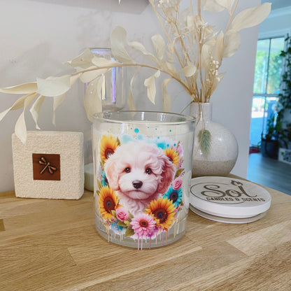 Candle with a Cavoodle dog and flower design on a wooden surface with decorative elements.