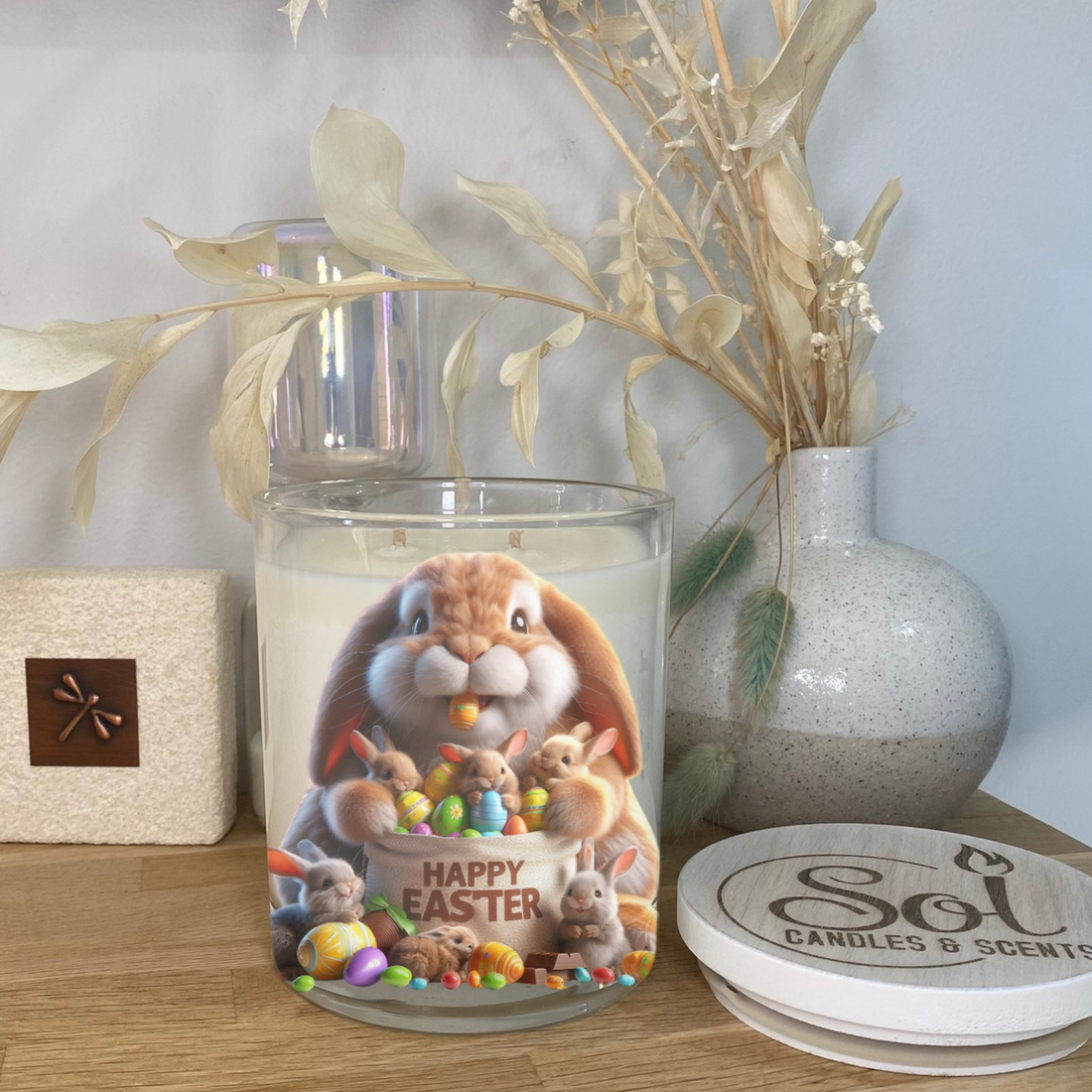 Decorative candle with Easter design on a wooden surface, featuring a rabbit and eggs.