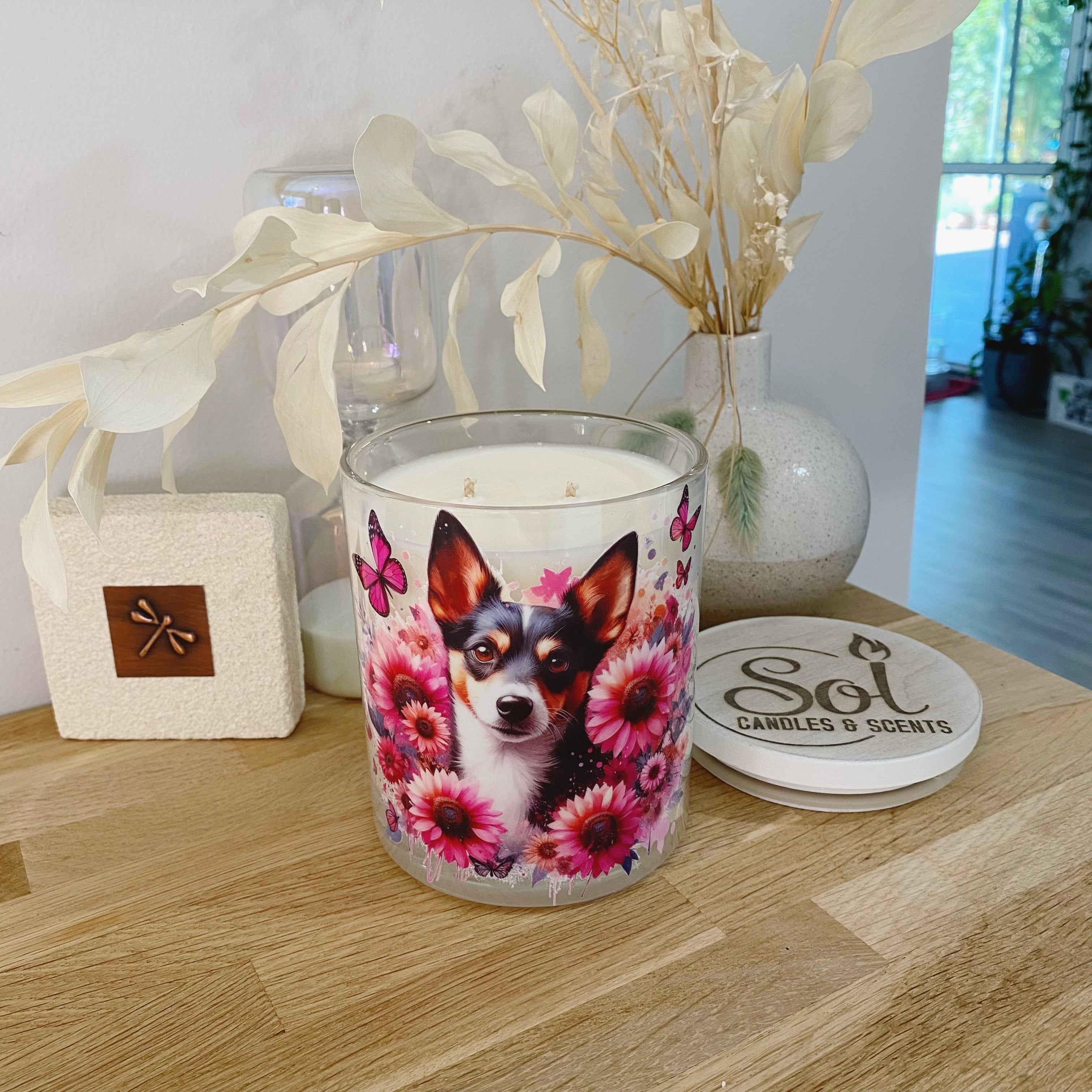 Candle with a dog design on a wooden surface, surrounded by decorative elements.