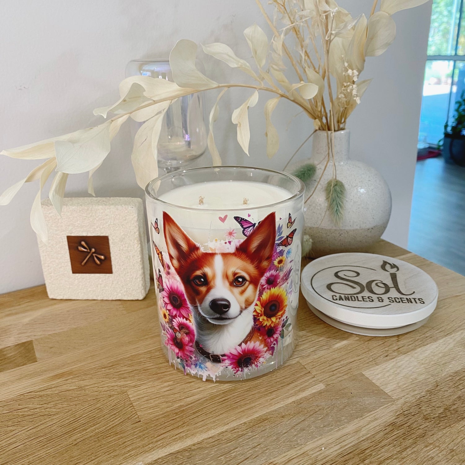 Candle with a Foxie dog design on a wooden surface, surrounded by decorative elements.
