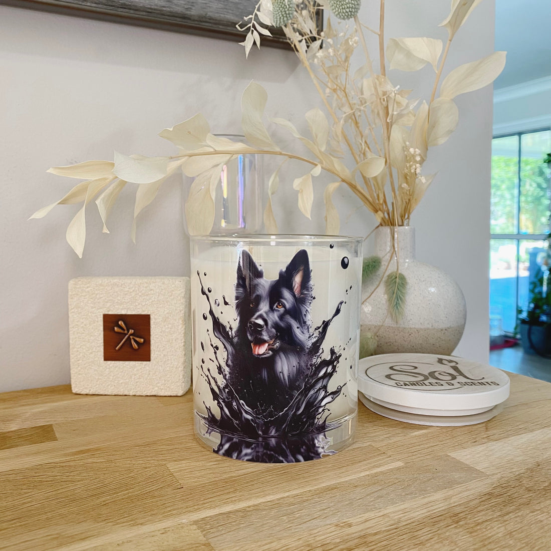 Xlarge candle featuring a black ink splash design with a German Shepherd, placed on a wooden table next to decorative elements.