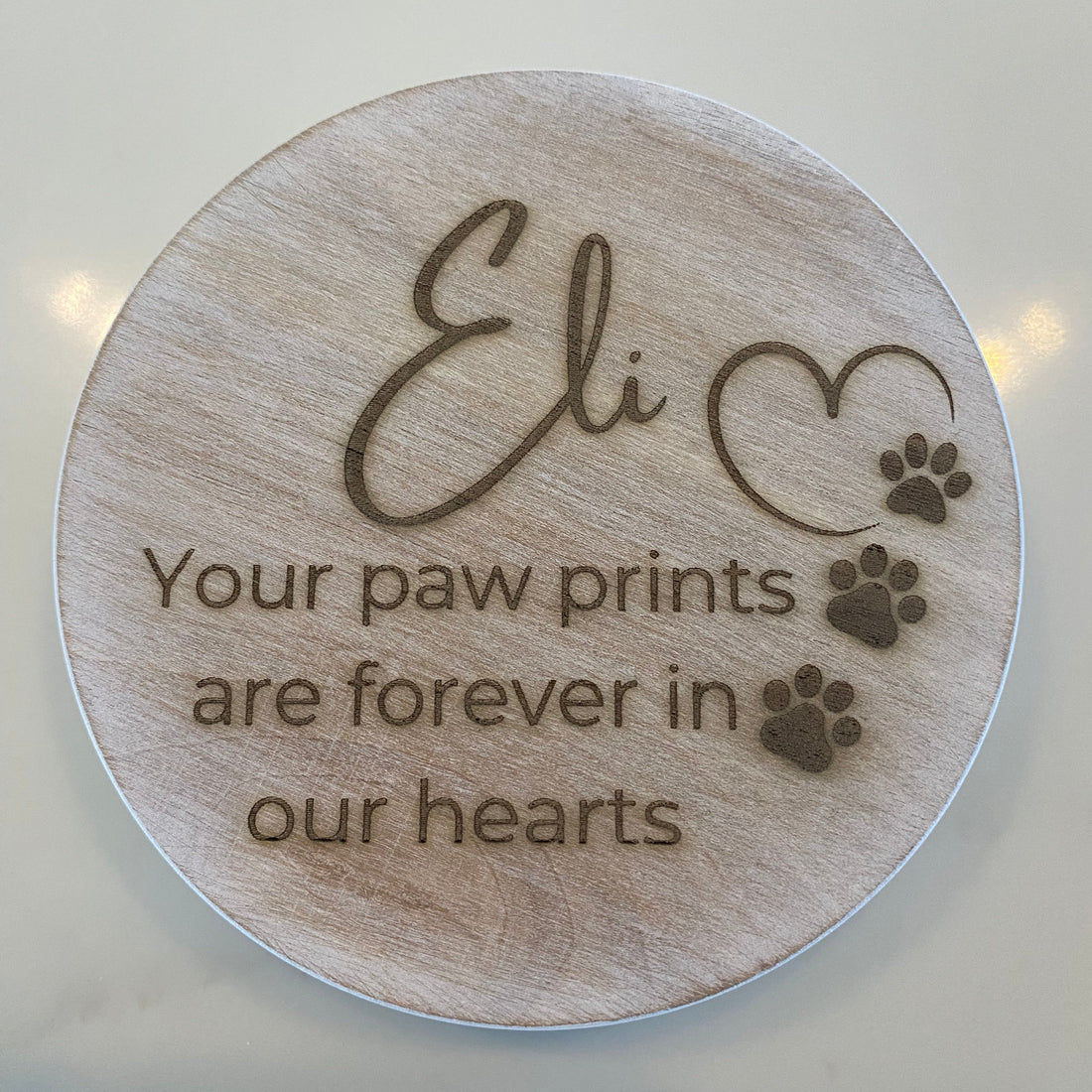 Round wooden candle lid with engraved text and paw prints on a light background